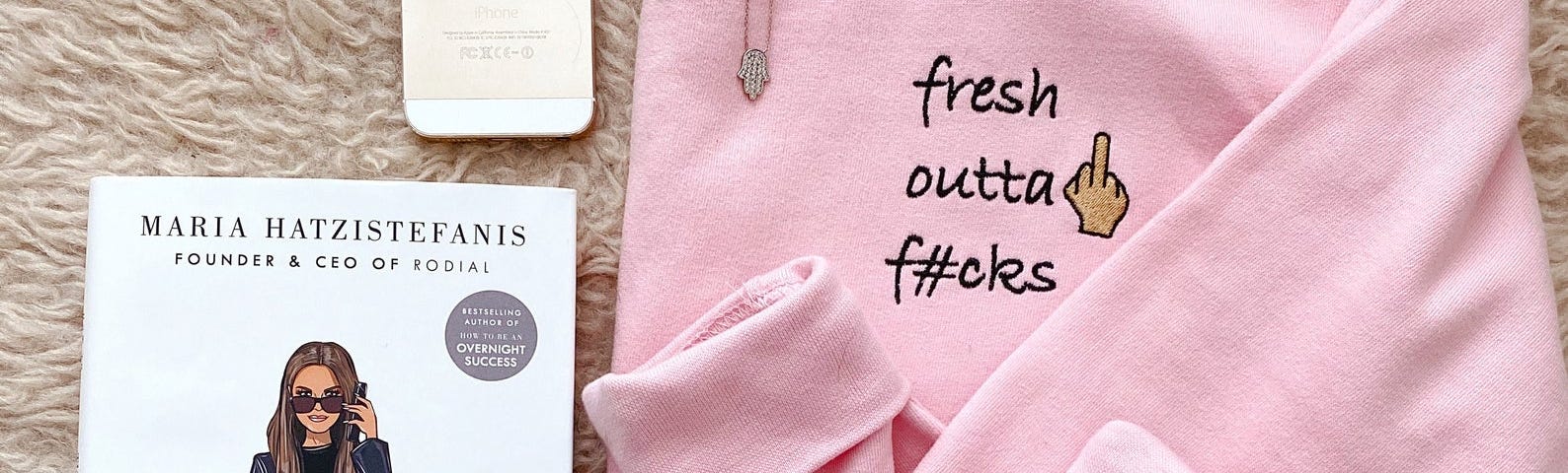 A pink jumper lay folded, written on it is “fresh outta fucks”. A phone and the book “How to Make It Happen” sits next to the jumper.