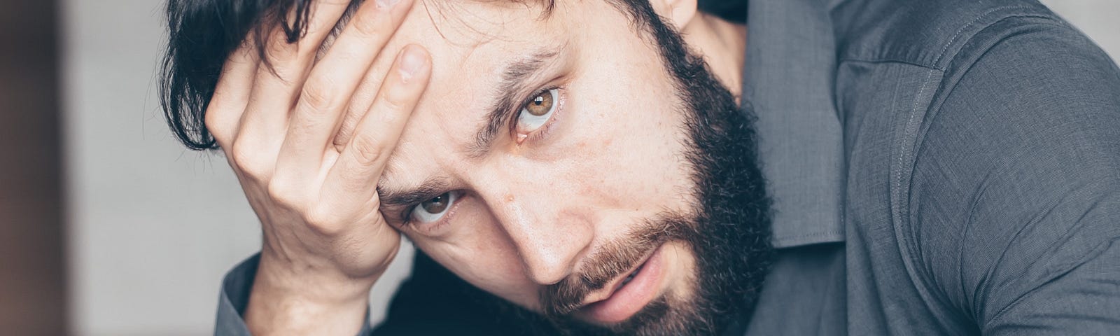 Man in gray shirt with hand on forehead