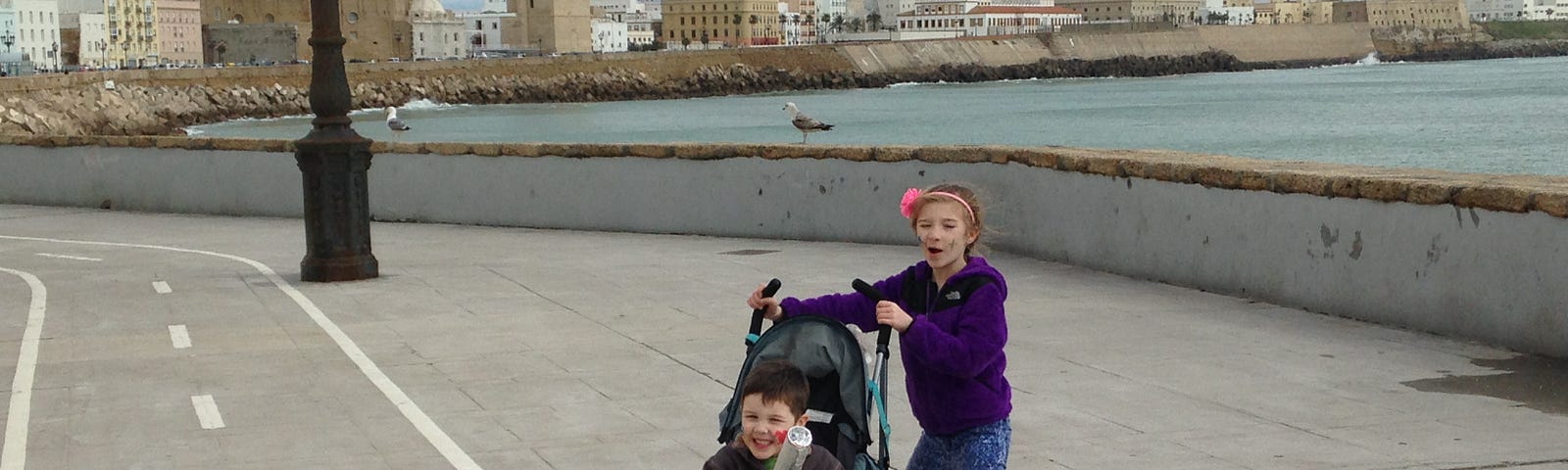 A young girl pushes her 5-year-old brother in a stroller in the waterfront area of Cadiz, Spain.