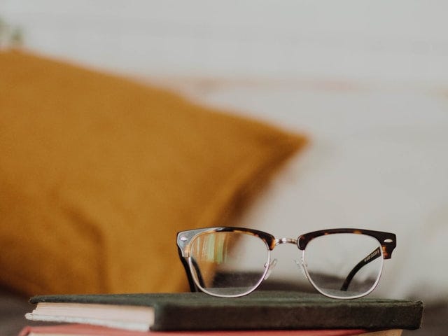 A pair of tortoise shell-rimmed eyeglasses rests on top of a stack of books.