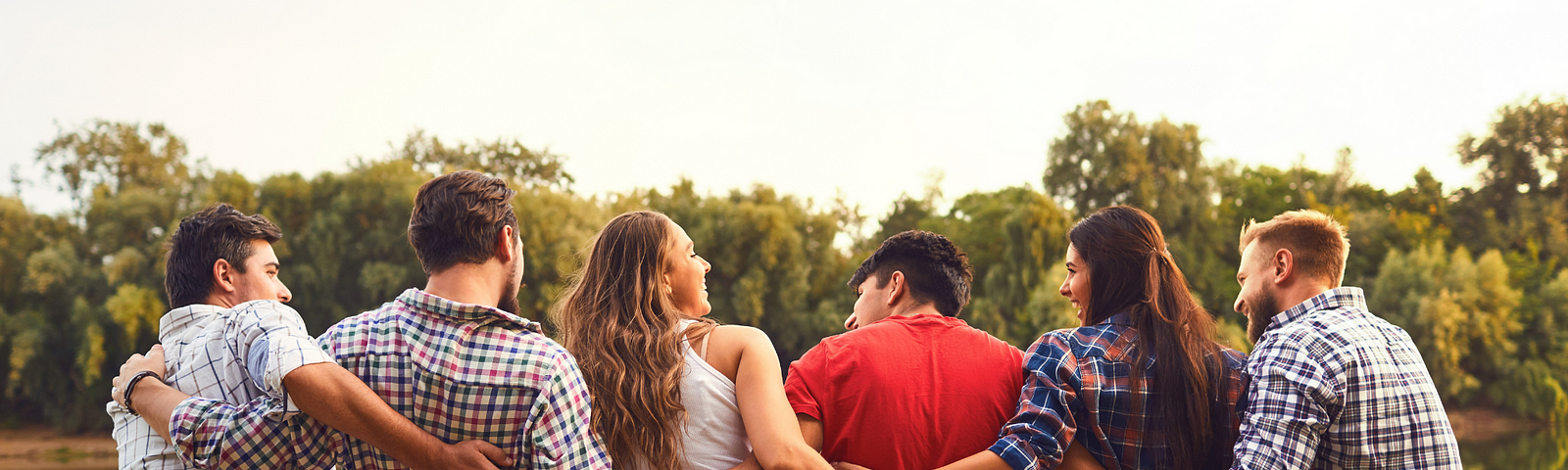 A group of young people sitting in grass with their backs to the camera — all linked with their arms around each other smiling. At the bottom of the image, the words “you are welcome here”