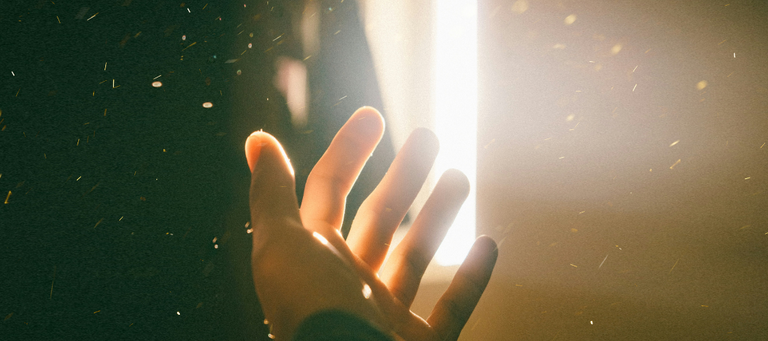 Left hand palm close-up as beams of sunlight illuminate dancing dust motes.