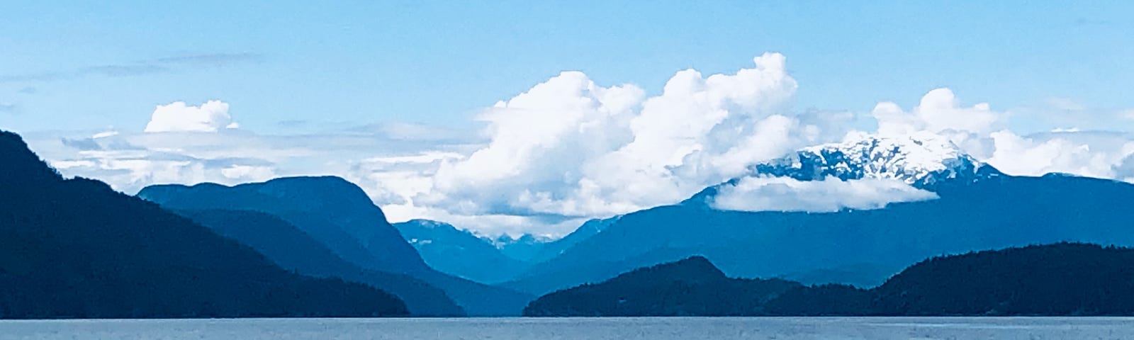 The ocean fronts a mountain range with fluffy white clouds behind it