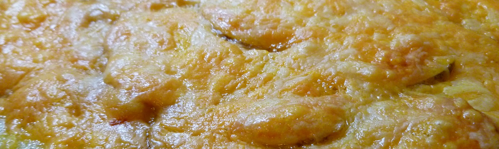Close up of sliced potatoes with cheese baked in round metal baking dish.