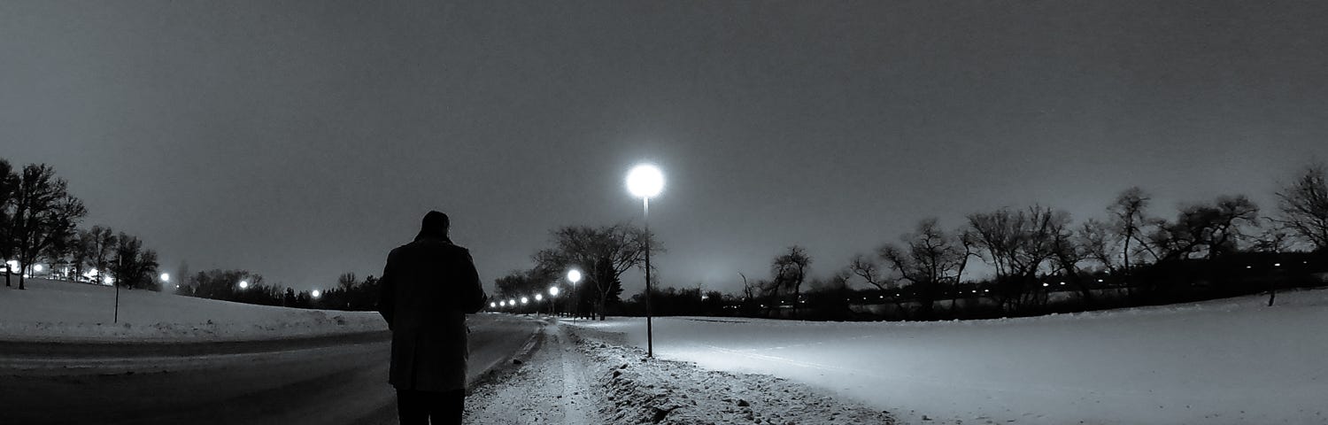 I am walking down a snow-plowed path that is lit with lanterns