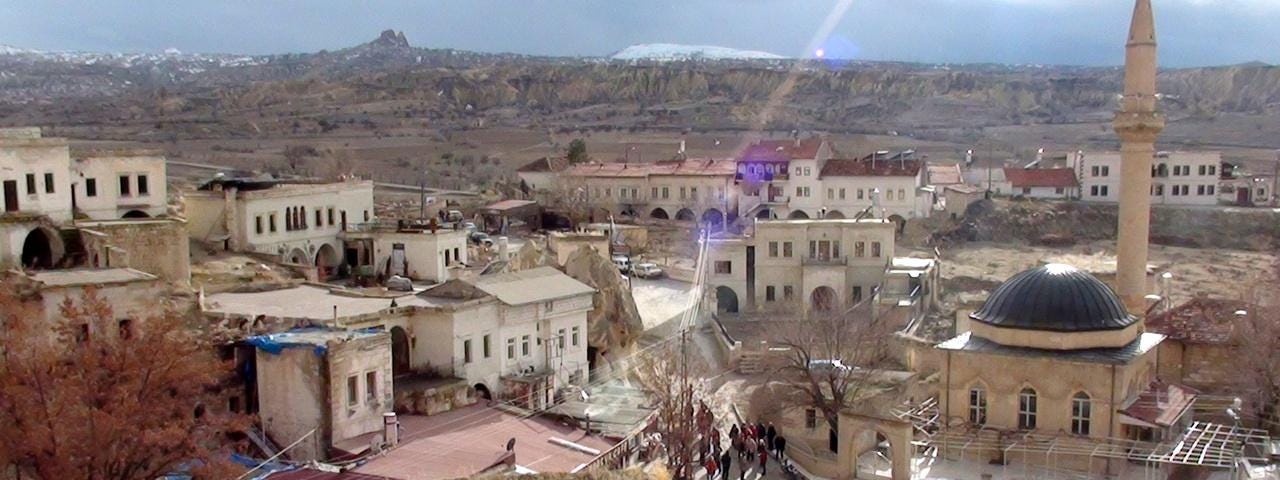 Cappadocian village with a mosque and white buses waiting for the tourists.