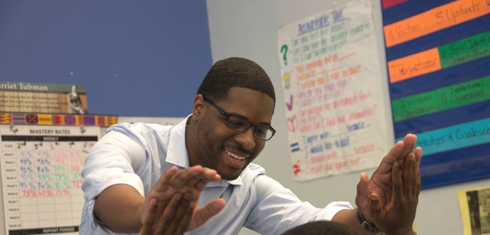 A teacher in a white shirt giving a student a double high five