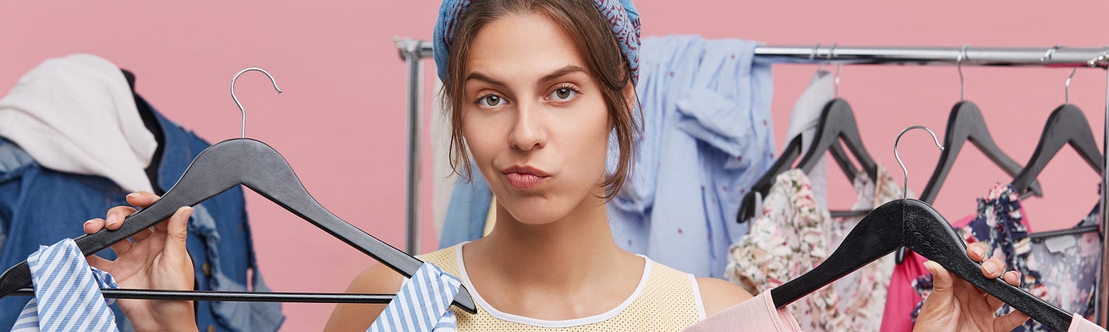 The woman looks at the camera, she carries two shirts the first one is blue and the other one is pink.