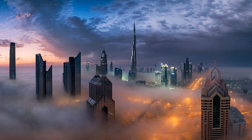 Tops of skyscrapers above cloud-covered city at dusk