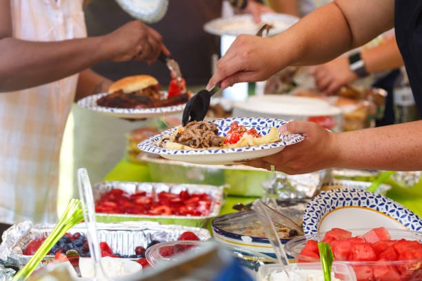 An array of food at a potluck with people serving it onto plates.