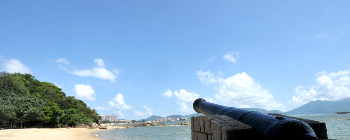 An antique canon on the right-hand side facing towards the beach at the far end under the blue sky.