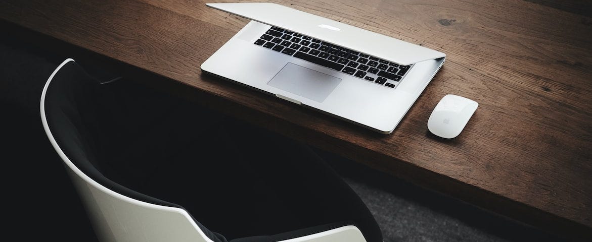 A photo of a white and black chair, brown desk, and grey/black laptop. Photo by Luca Bravo via Unsplash