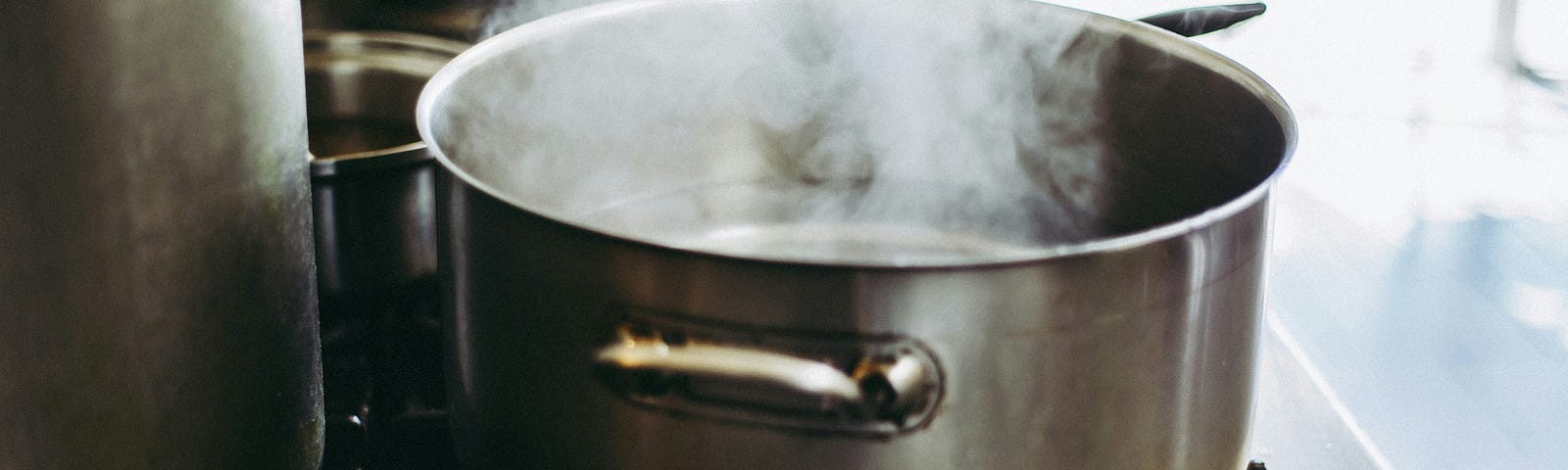 A silver pot with clear liquid and steam coming out of it