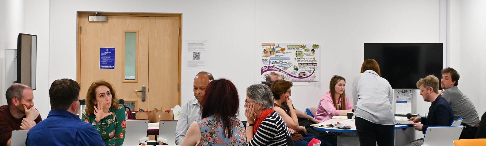 Researchers and facilitators sit in discussion around tables at one of the collaborative lab sessions