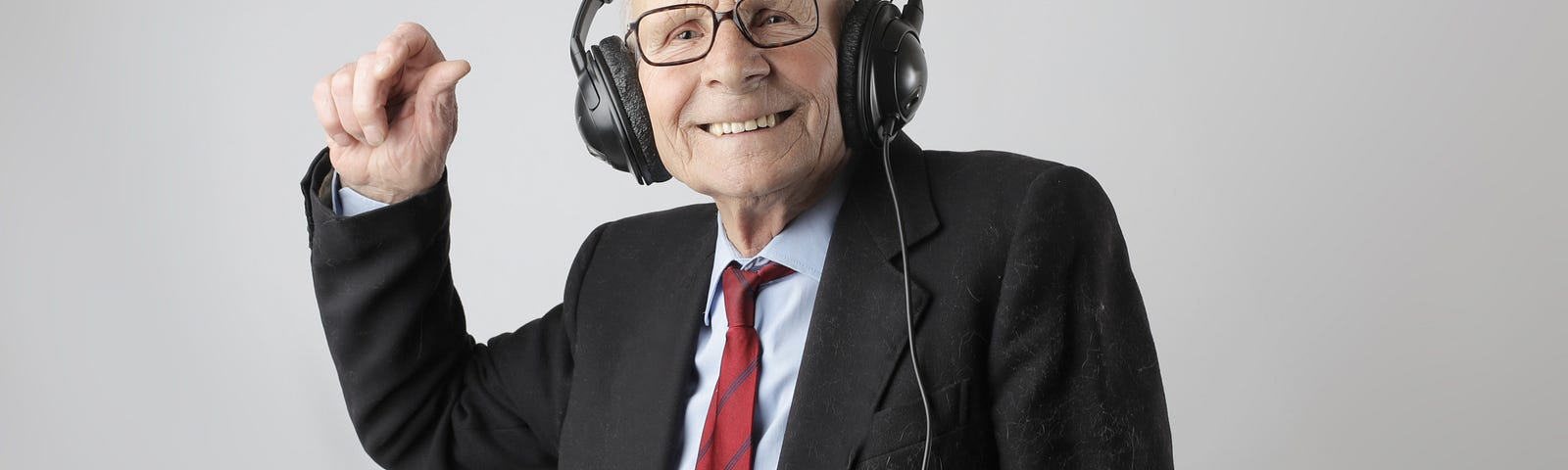 Old man in a suit listening on headphones and smiling and grooving