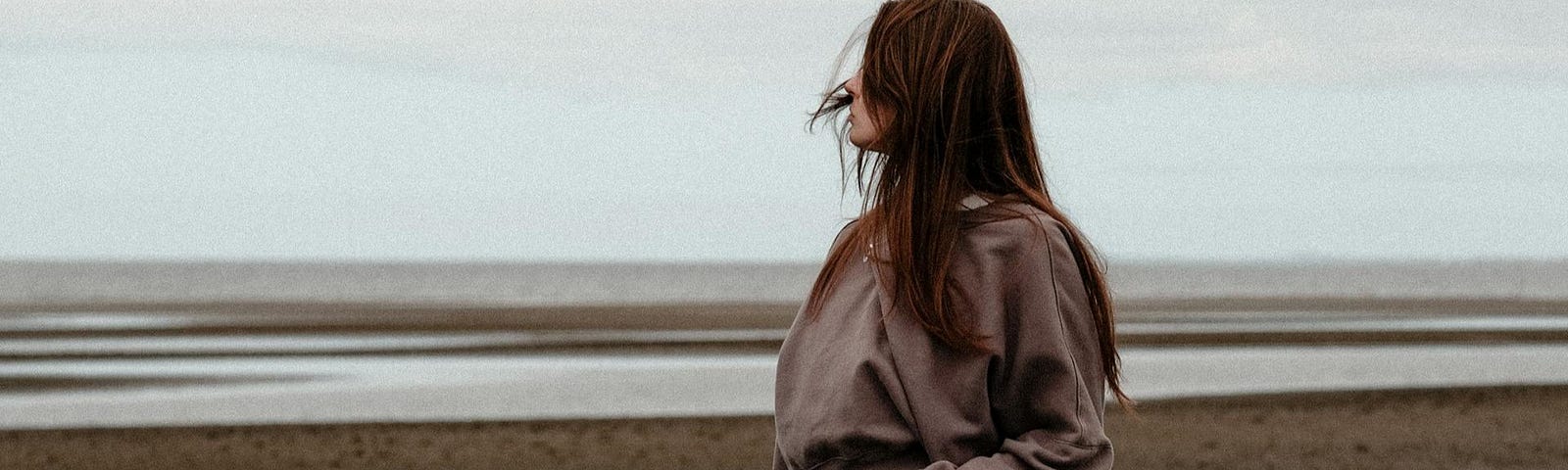 A woman standing on the beach looking contemplatively out onto the water