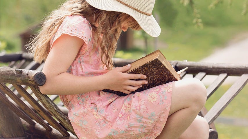 A young girl sitting on sn old bench reading a book.