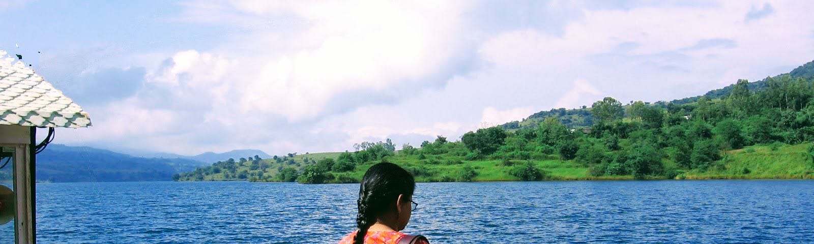 Woman gazing at a boat in the water with mountains and greenery in the distance