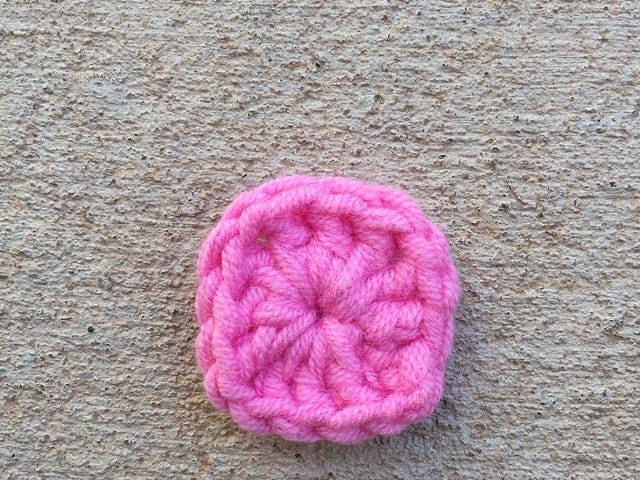 The first round of a granny square made with pink worsted weight yarn and a 5.00 mm crochet hook
