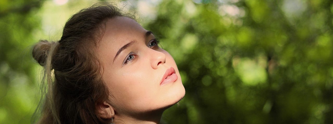 Young woman in a natural setting gazing off into the sky as if daydreaming.