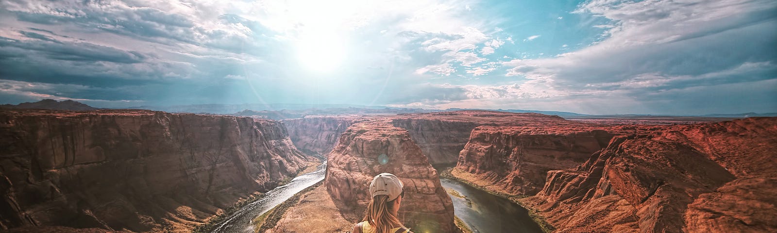 Woman looking out over canyon admiring the view with water below and the sun shining brightly overhead.