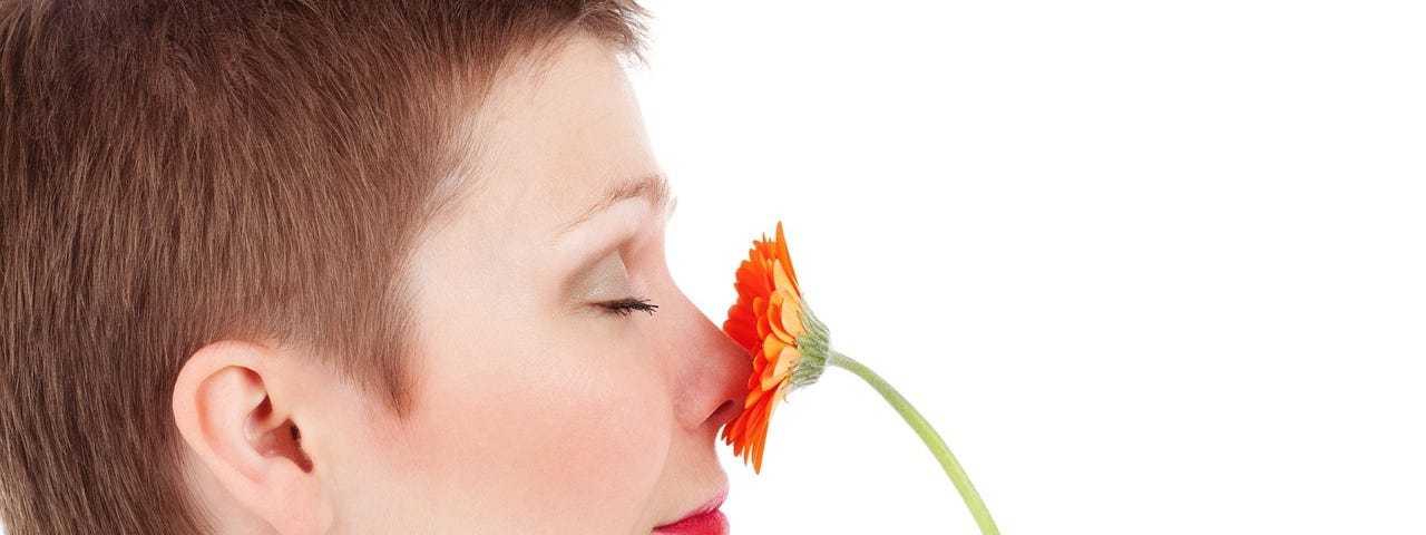 Woman, with eyes closed, smelling a gerbera daisy.