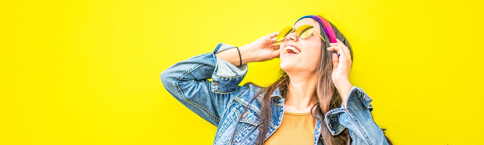 Young women in sunglasses looking up and smiling in front of a bright yellow background.