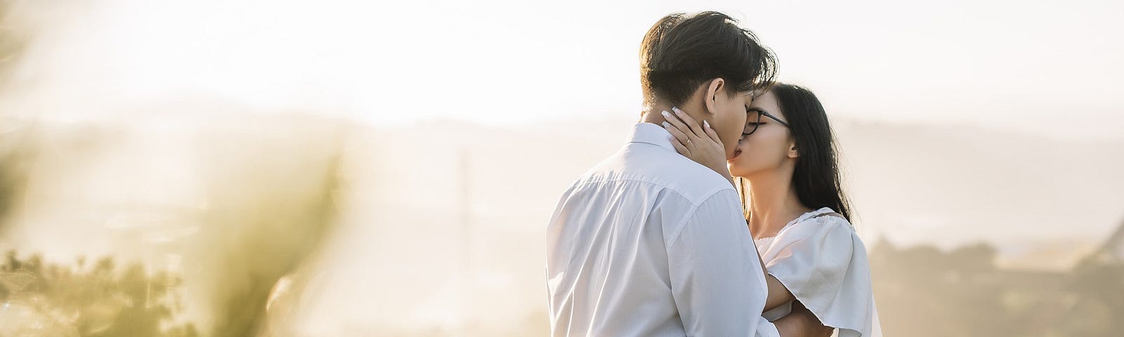 A young couple kiss in a soft focus field of flowers.