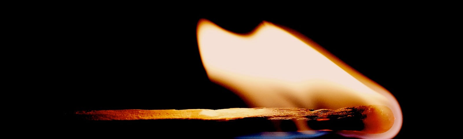 A lit match with a flickering flame extending out of the darkness