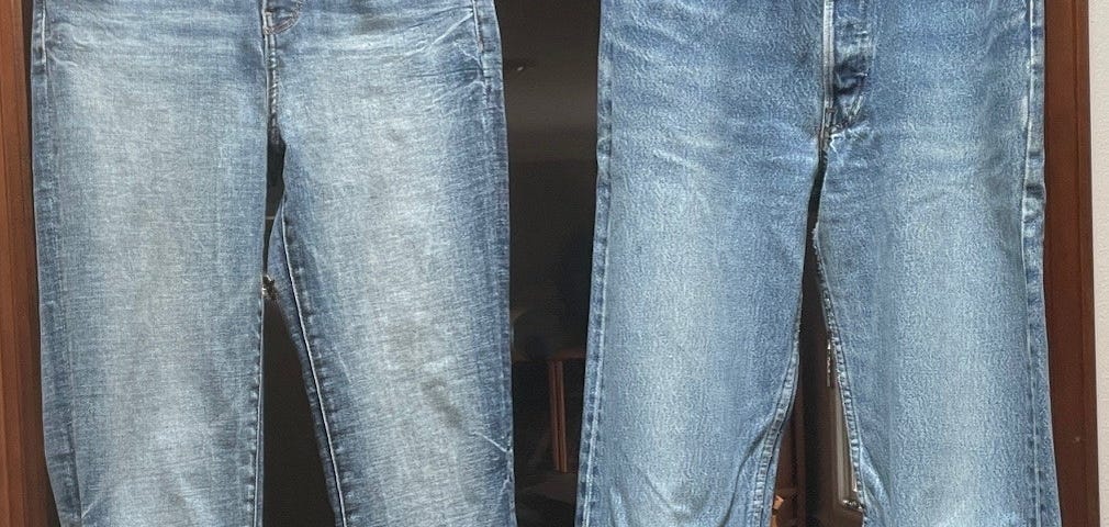 Two pairs of faded blue jeans hang from a door frame