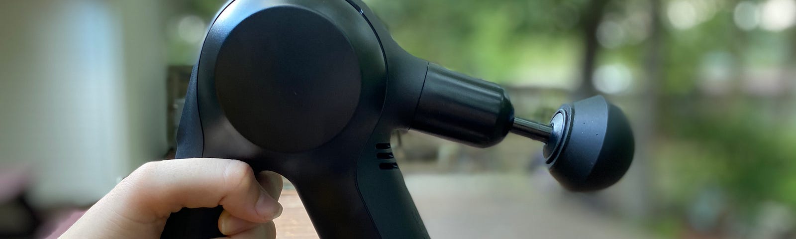 A close-up of a person holding a massage gun outside.