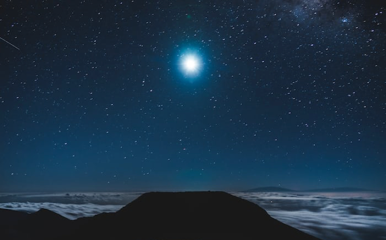 Photo of full moon over ocean and land.