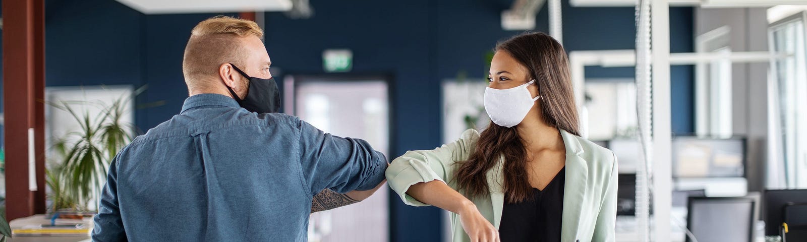 Two masked individuals elbow one another in an office.