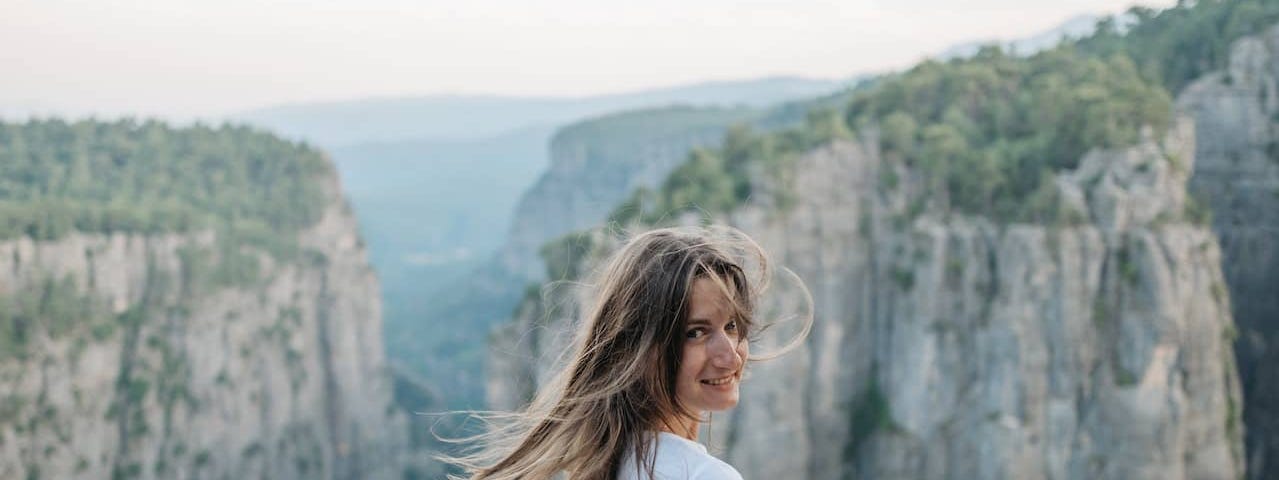 a woman on top of a cliff looks at the camera with wind in her hair smiling because she took the leap into a sex coaching career