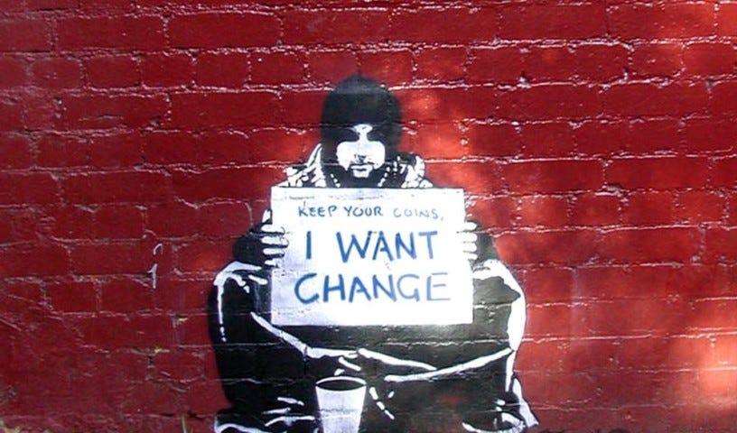 Homeless man painted on a brick wall with sign “Keep your coins, I Want Change.”