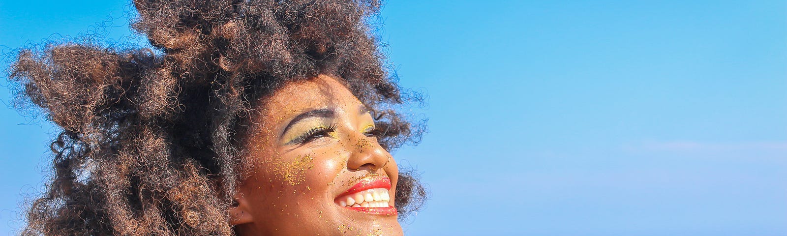 A woman smiles into the sun on the beach.