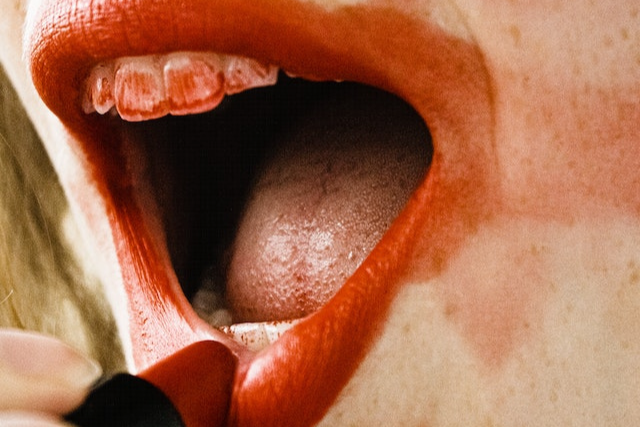 A woman putting red lipstick on her bottom lip, lipstick smeared on her teeth and side of her mouth.