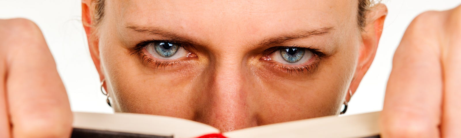 A woman looks directly at us over the top of a book she has been reading. It is clear she is unhappy with what she has just read.