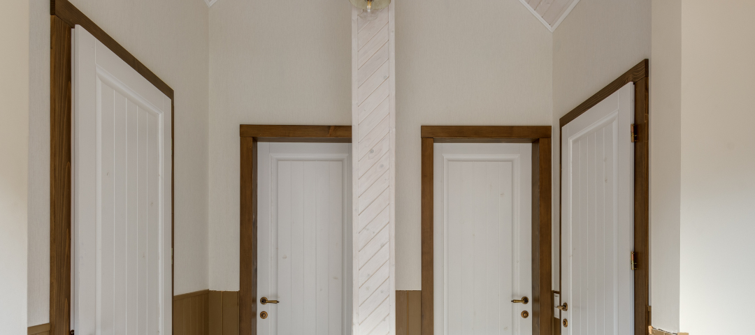 Within a two-toned hallway of white and brown, are four white doors. Two are across from each other. Two are directly next to each other.