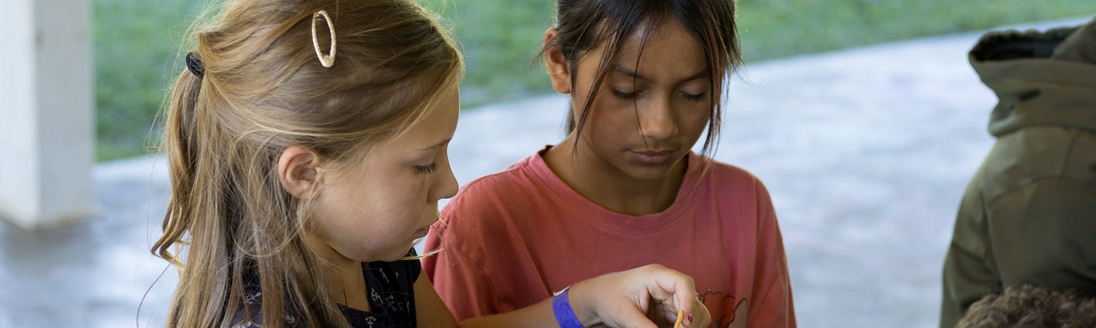 Two young girls are sitting at a camp table, focused on doing arts and crafts.