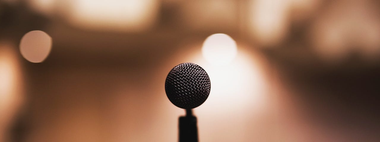 A microphone sits ready on an open stage with a spotlight