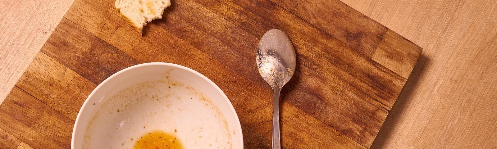 A bowl of soup that is nearly empty with a spoon nearby.