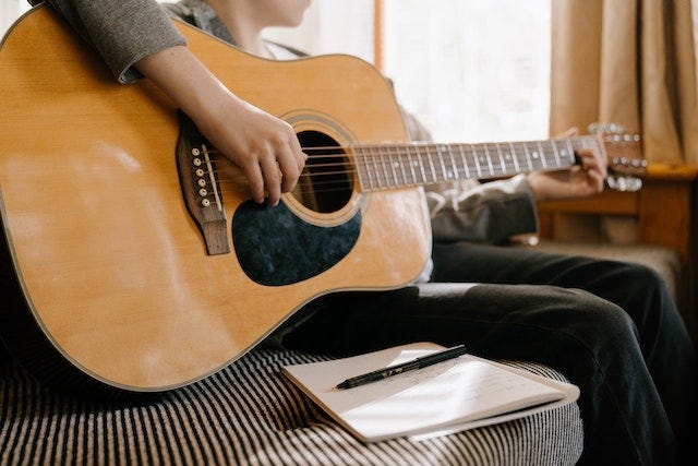 Person playing an acoustic guitar with a notepad and pen next to them.