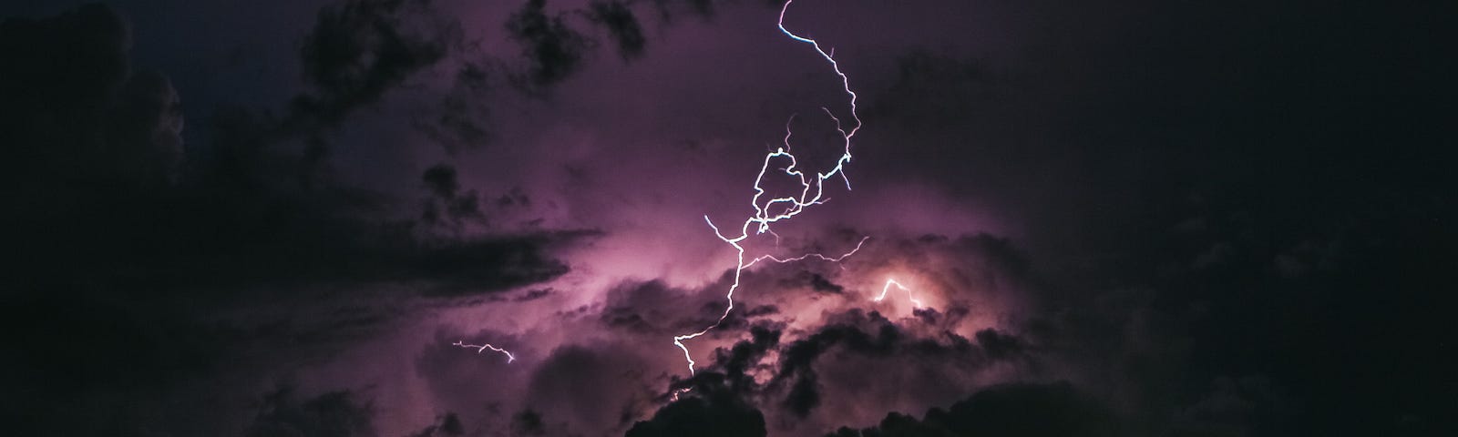 A dark sky full of clouds is lit up by a single lightning bolt in the centre of the scene.