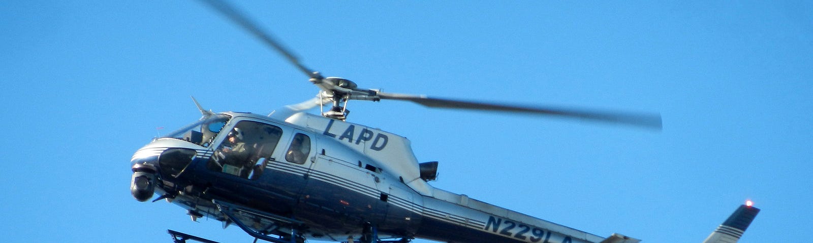 LAPD Police helicopter in flight, with blue sky behind it.