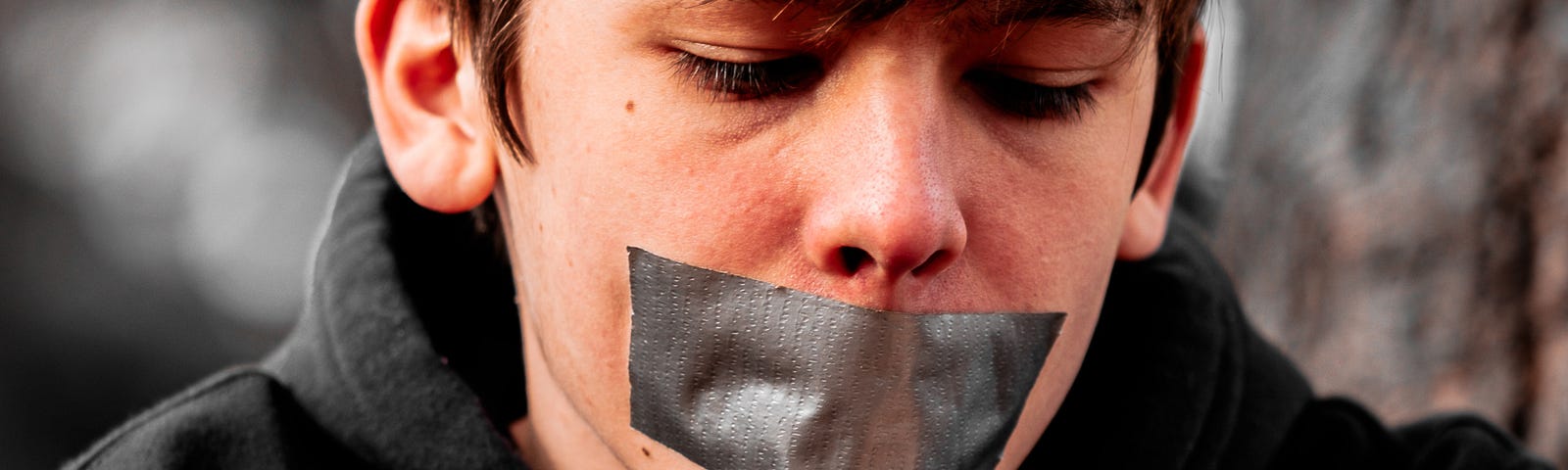 Boy with tape over his mouth in black sweatshirt.