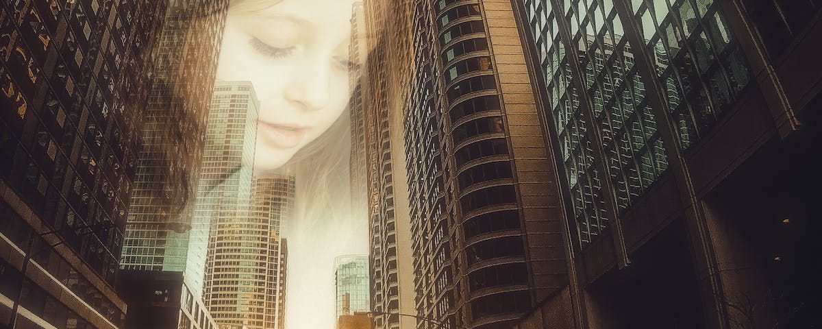 A city street, a canyon between skyscrapers, at sunset. The sun sets at the end of the road. The translucent face of a girl fills what sky is visible in the narrow gap between buildings.