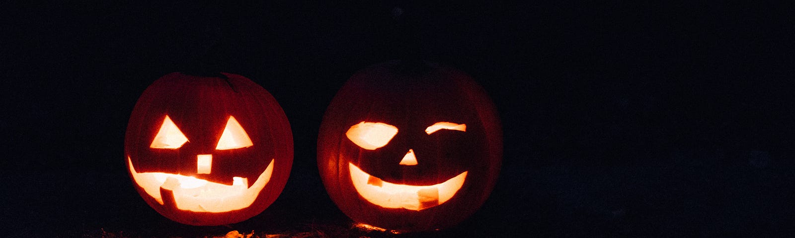 An image of two jack-o-lanterns (pumpkins with faces carved into them) in the dark lit up.