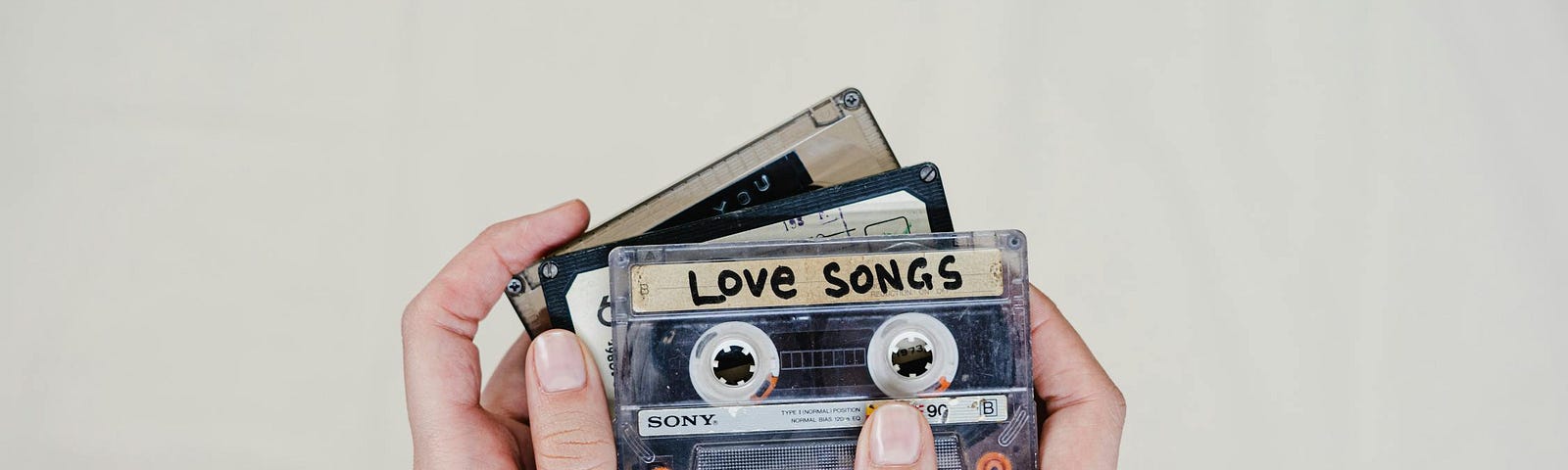 A pair of hands holding a cassette tape with ‘Love Songs’ handwritten on the label