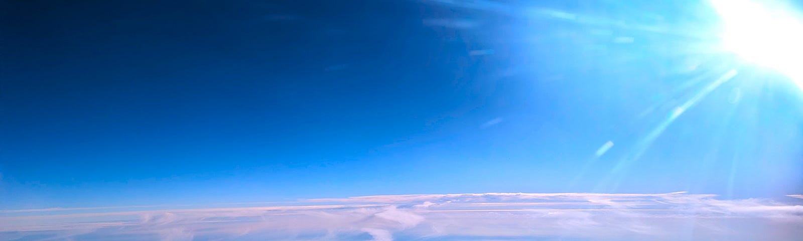 This shows a blue sky above white clouds with the sun off to the right. It was taken from an airplane window.